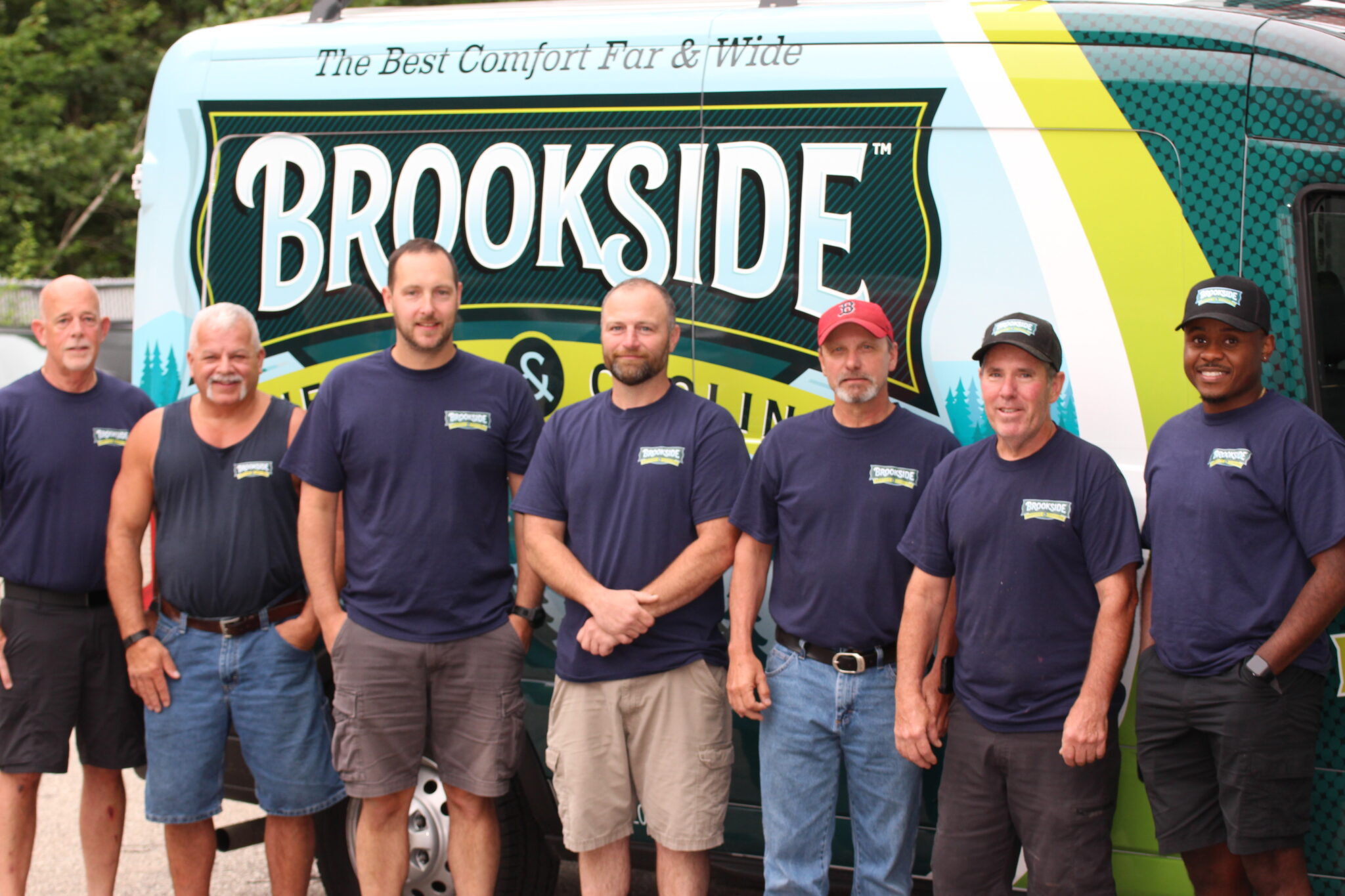 Seven male team members in matching navy Brookside branded shirts standing in front of a white and teal RV with yellow